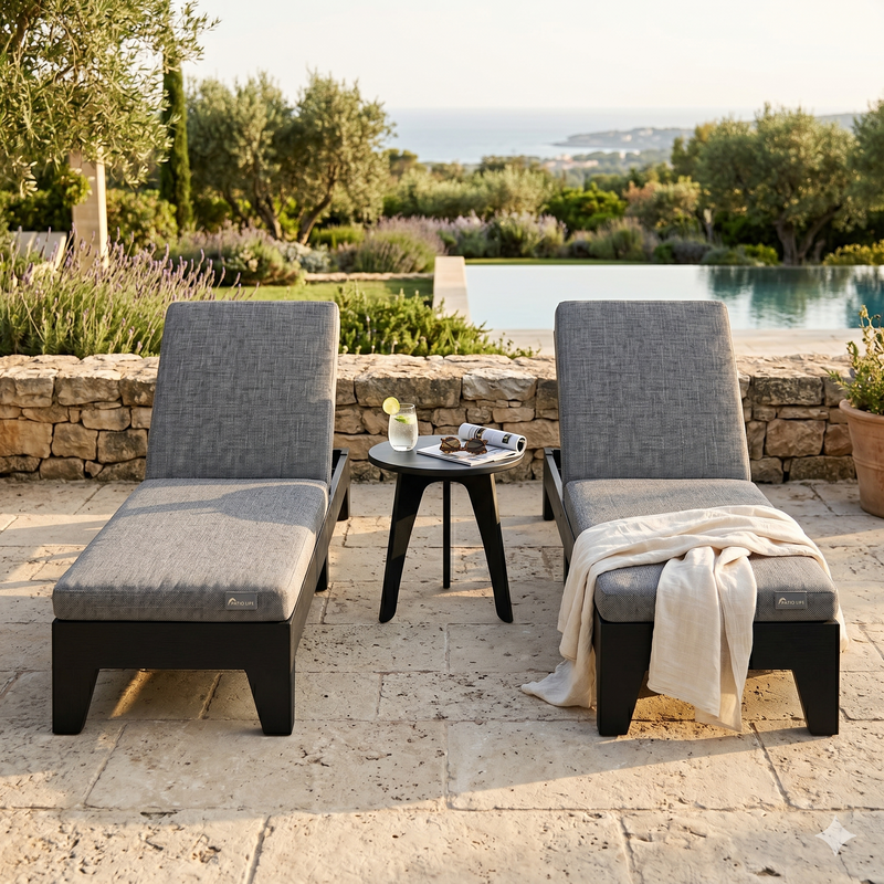 Two gray outdoor lounge chairs with a small table by a poolside, surrounded by greenery.