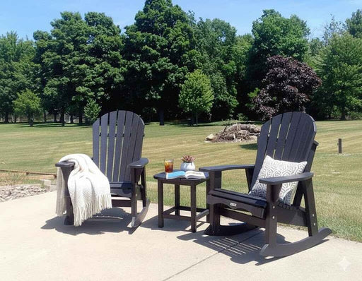 Two Krahn poly Adirondack chairs with a small table on a patio area with trees in the background.