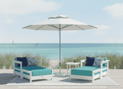 Krahn outdoor furniture patio set with two deep seat armchairs with matching ottoman, a krahn side table, and an frankford greenwich market umbrella on a beach.