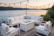 Outdoor patio set with sectional sofa, chairs, and fire pit table by a lake at sunset.