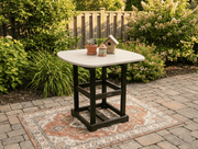 Krahn poly outdoor bistro table with decorative items on a patio surrounded by greenery