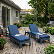 Two poly chaise lounge chairs on a wooden deck with a house and garden in the background.