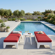 Outdoor poolside setting with red cushioned lounge chairs and a small table by a pool.